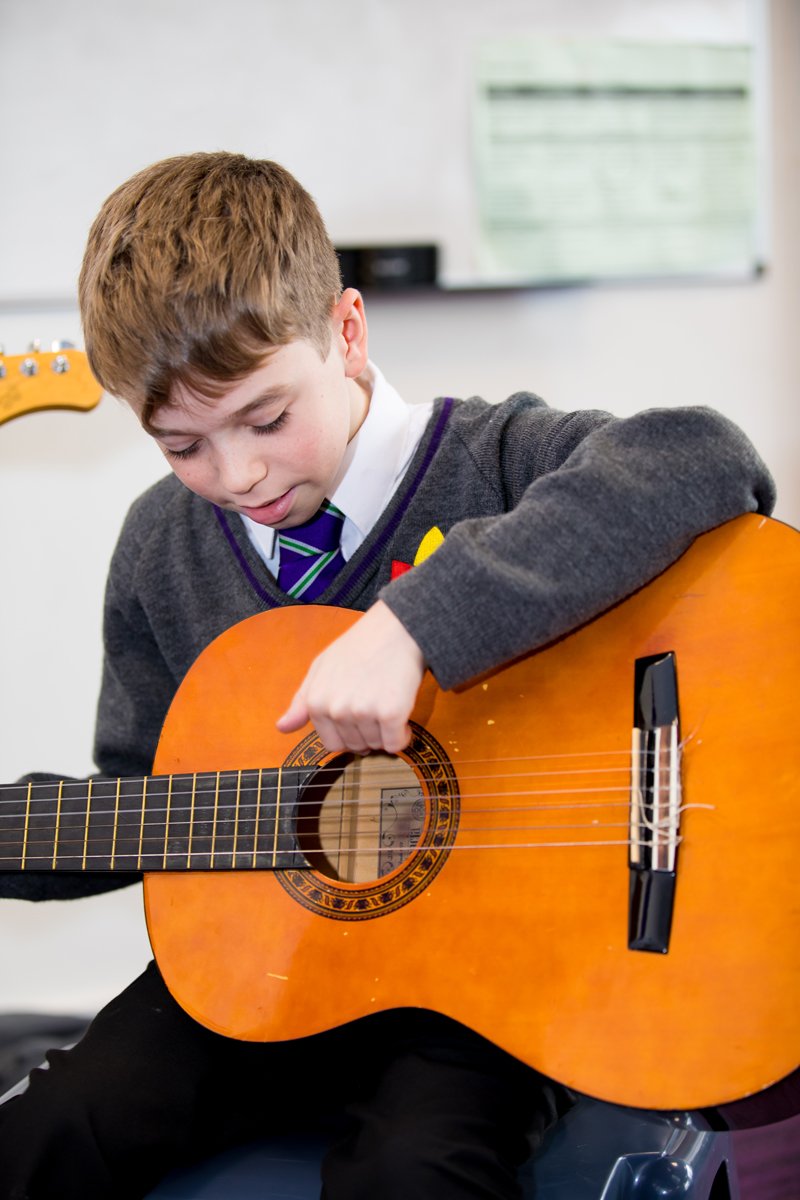 A student holding a large wooden guitar and playing it