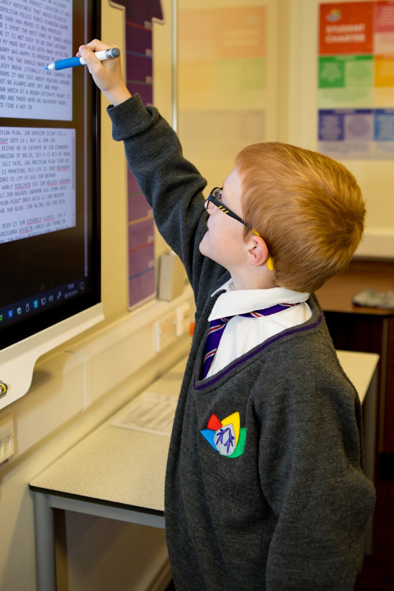A student reaching up to a smartboard with a pen in his hand