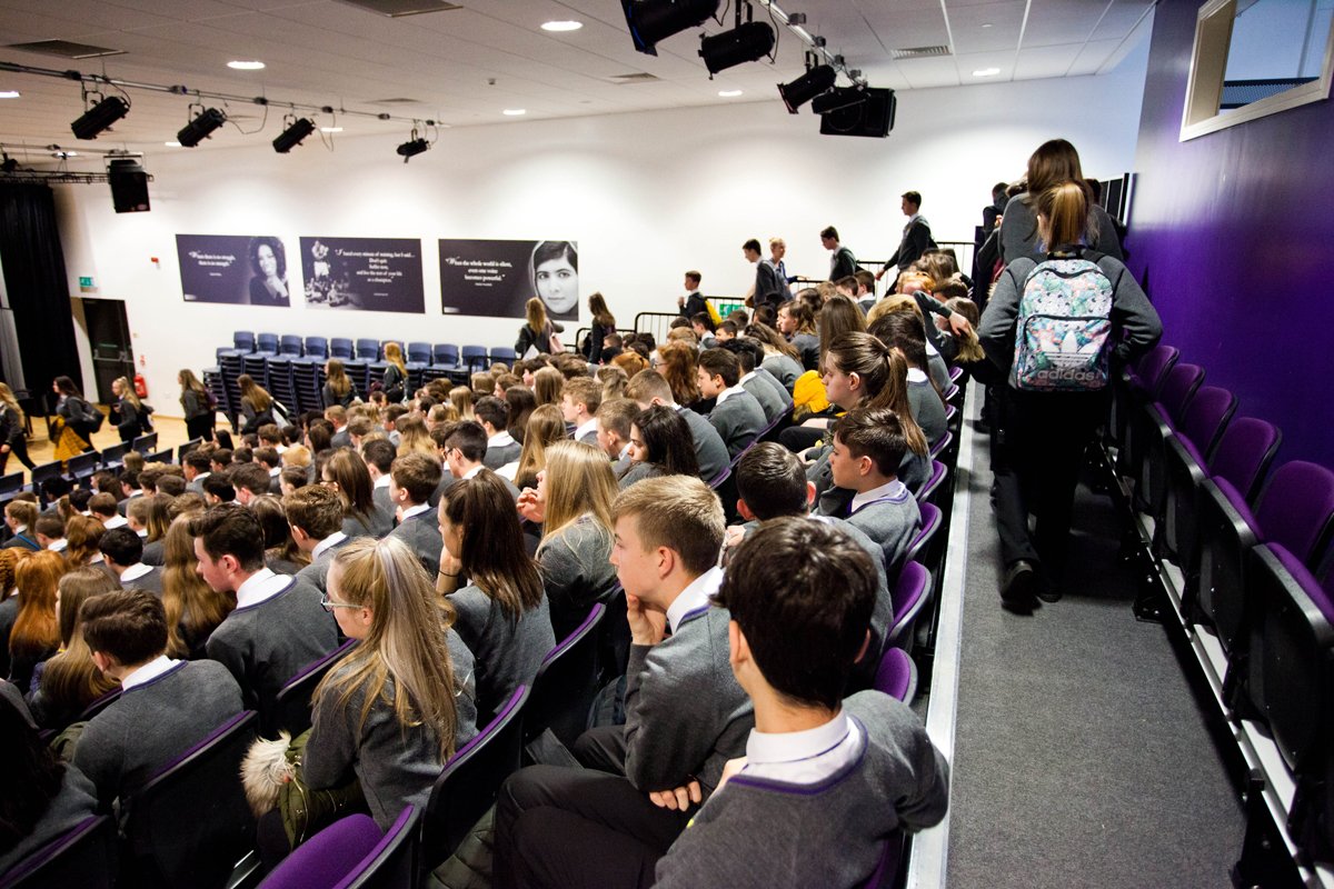 A wide photo of students sat in the main hall, most of the seats are full