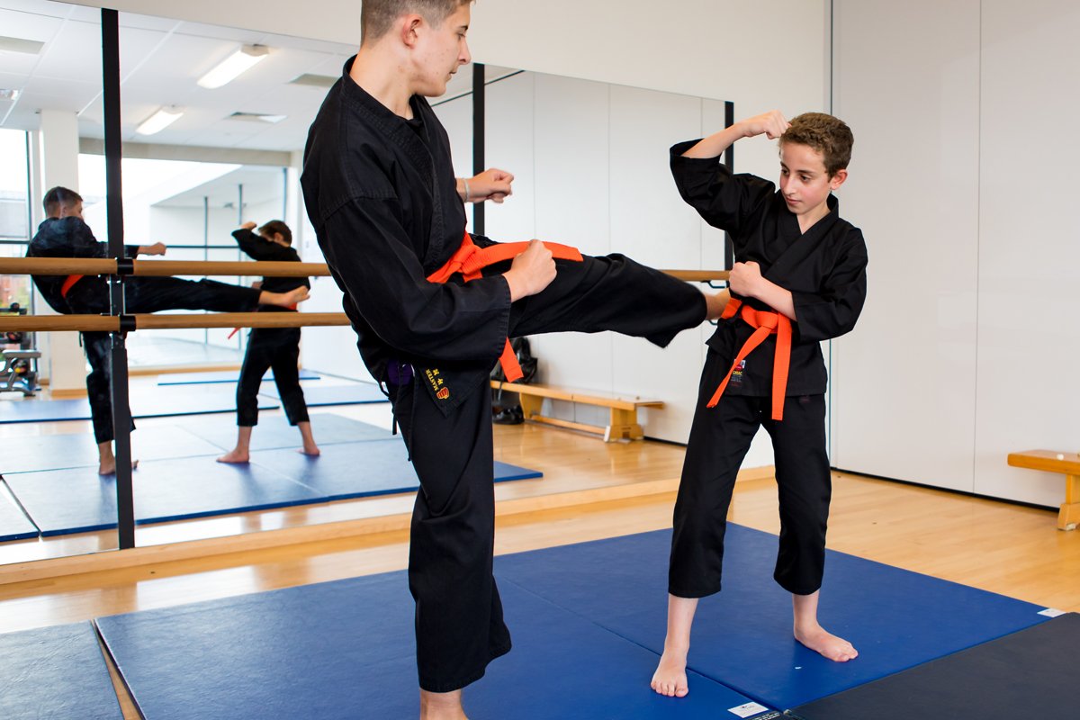 2 students in a karate lesson, one has their leg raised to kick the other