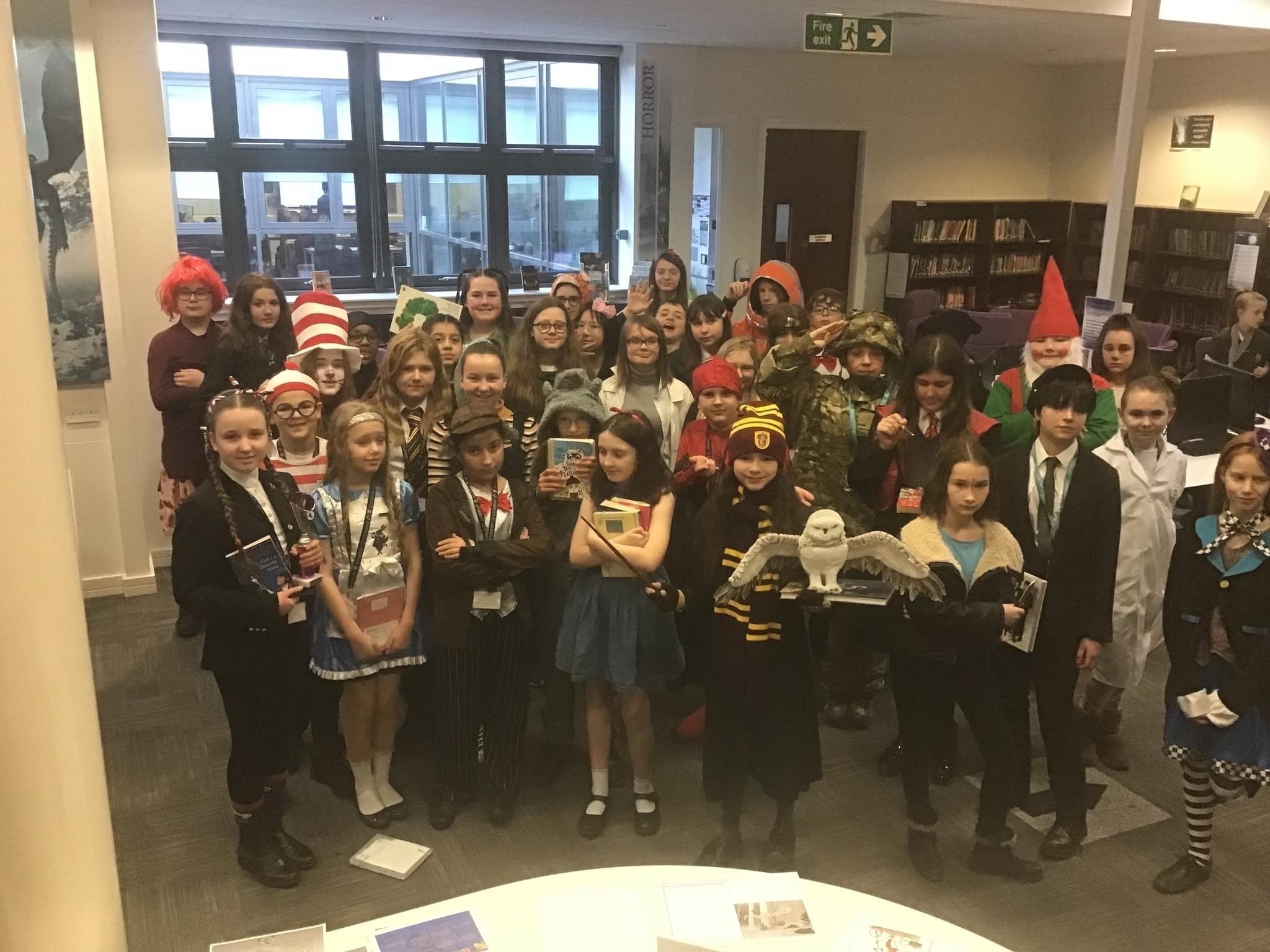 A large group of 20-30 students stood together, they are wearing a variety of costumes for world book day